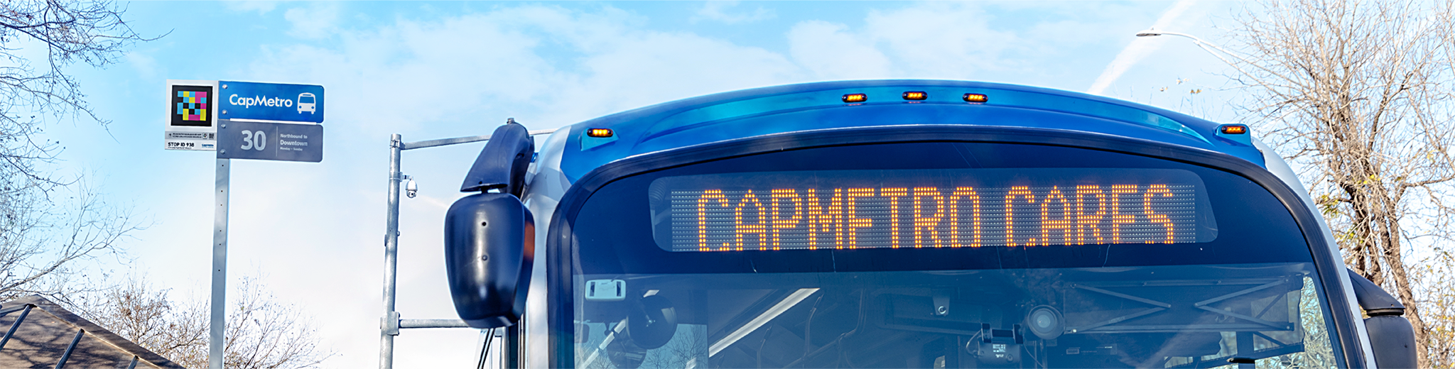 Photograph of a CapMetro bus sitting next to a bus stop sign with a NaviLens code on it.