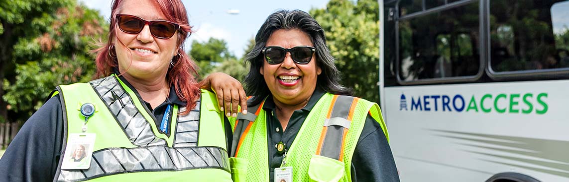 Two female MetroAcess driver smiling while standing beside a MetroAcess vehicle