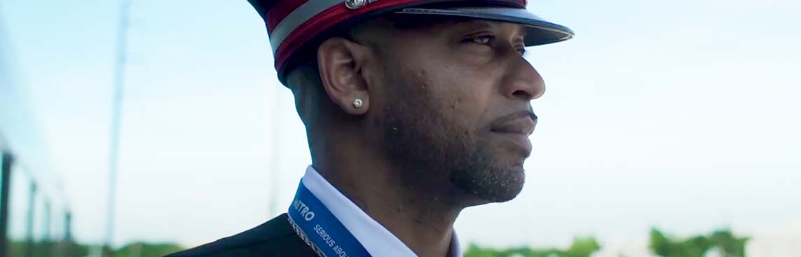 CapMetro rail conductor looking off into the distance as a MetroRail vehicle goes by behind him