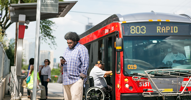 Person looking at phone next to bus stop while person using a wheelchair boards a MetroRapid bus