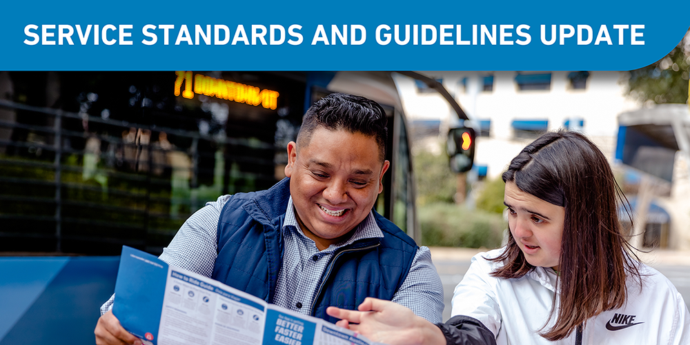 Three adults at a bus stop looking at a bus system map while standing in front a blue CapMetro bus.