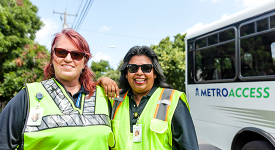 Two female MetroAcess driver smiling while standing beside a MetroAcess vehicle
